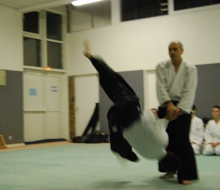 Photo en mouvement : un partenaire, jambes en l’air, chute à côté d’un pratiquant resté debout.